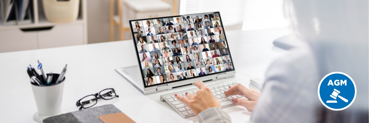 A woman sits at her desk typing on a keyboard with a virtual meeting showing a number of individuals on her computer screen.