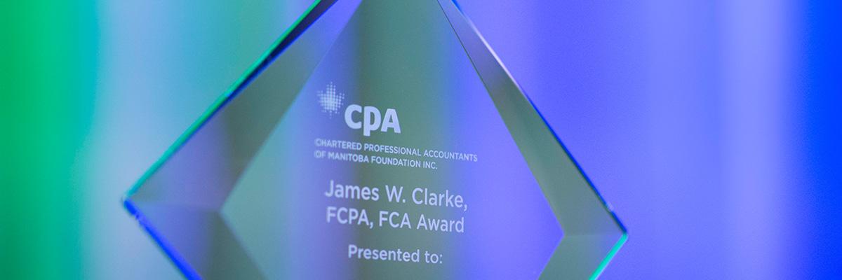 A glass, diamond shaped award with the CPA Manitoba Foundation logo on the top with the words James W. Clarke, FCPA, FCA Award Presented to on it.